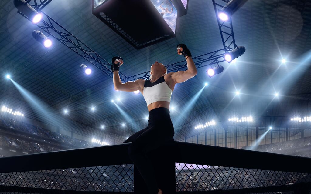 Lutadora de MMA comemora vitória sobre a grade do octogono