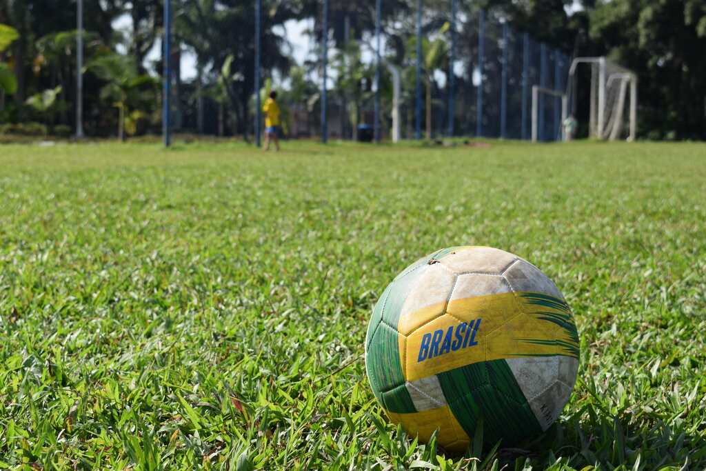 Bola de futebol com as cores do Brasil, e escrito Brasil em um vasto campo verde.