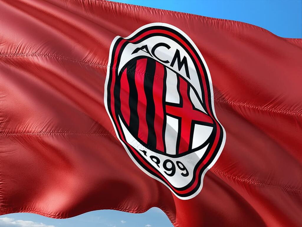 Bandeira vermelha com o escudo do AC Milan na frente, com um céu azul de fundo.