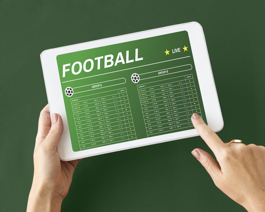 Tablet sendo segurado por uma mão esquerda, com uma tela de apostas esportivas aberta.
