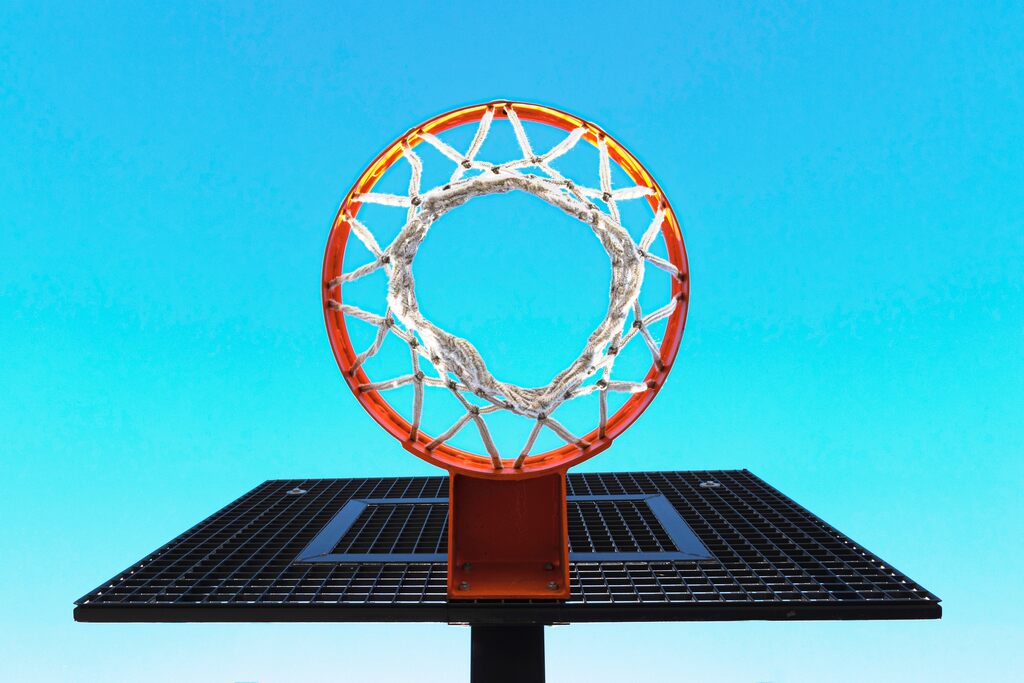 Cesta de basquete, com aro laranja e rede branca, vista bem debaixo da mesma com o céu azul de fundo.