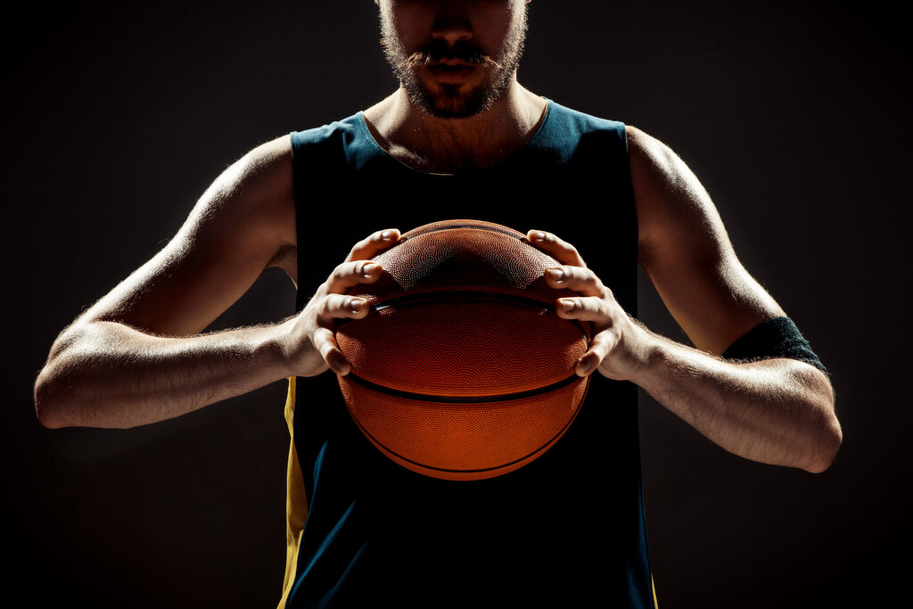 Jogador de basquete de blusa regata azul marinho, segurando a bola de basquete com as duas mãos na altura do peito.