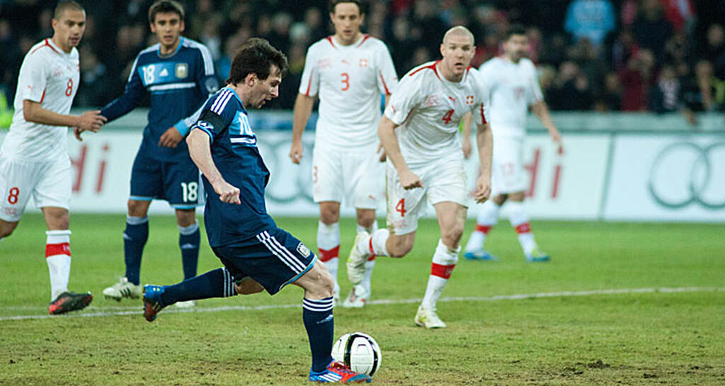 Lionel Messi batendo pênalti com a perna esquerda pela seleção argentina, com seu uniforme azul marinho.