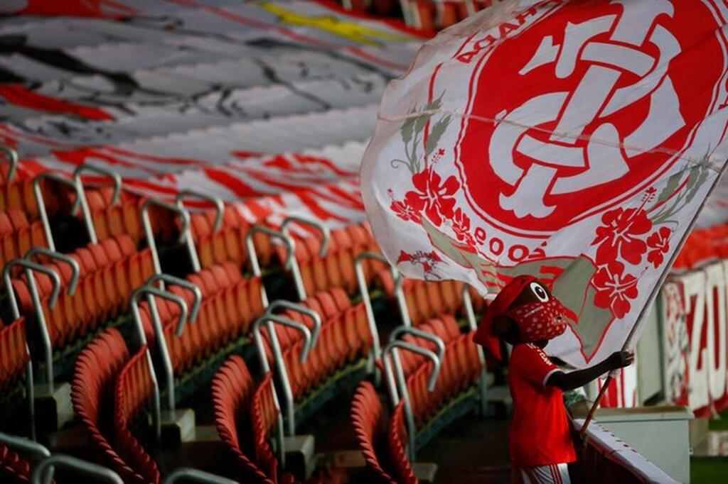 Torcedor do Internacional segurando a bandeira do clube na arquibancada do time, com cadeiras vermelhas atrás.