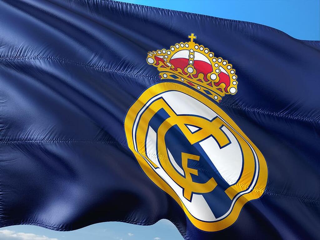 Bandeira azul marinho com o símbolo do Real Madrid no centro e um céu azul de fundo.