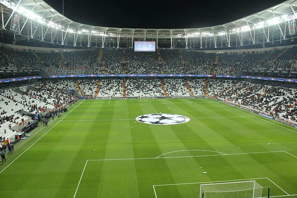 Estádio de futebol, com as arquibancadas ainda sem estarem totalmente cheias, e o símbolo da Champions League no círculo central.