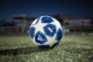 Uma bola de futebol da azul e branca, com estrelas da marca Adidas em um campo de futebol de grama verde