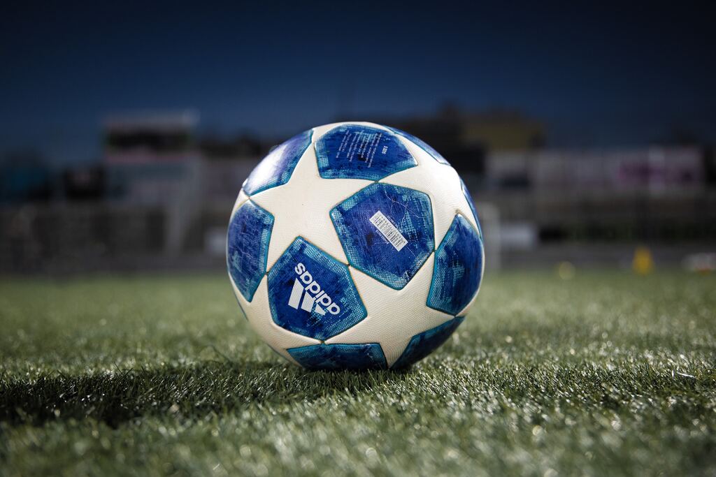 Uma bola de futebol da azul e branca, com estrelas da marca Adidas em um campo de futebol de grama verde