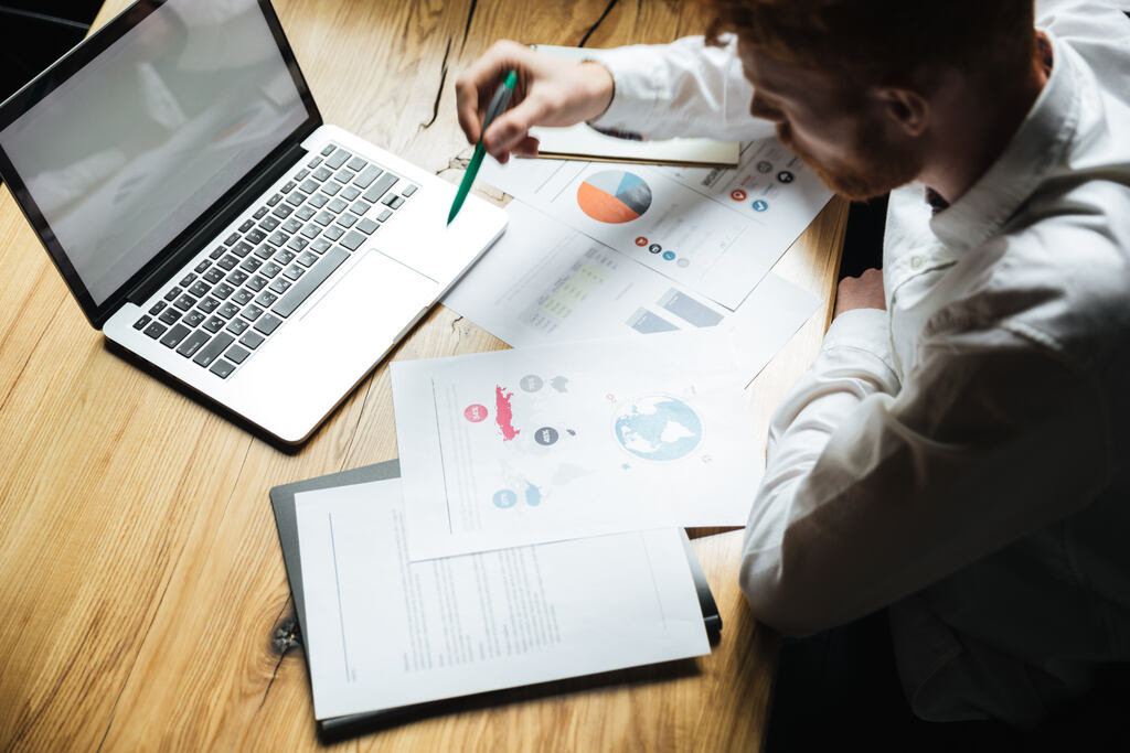 Duas pessoas analisando dados em um computador e algumas folhas na mesa com gráficos