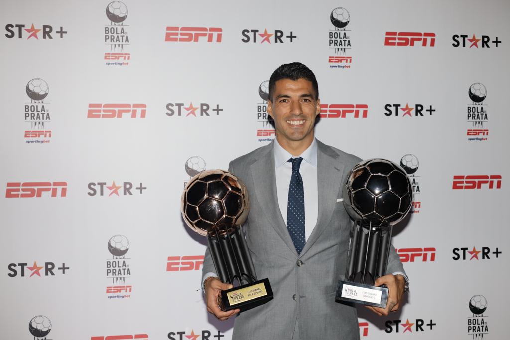 Jogador Luis Suarez sorrindo e segurando dois trofeus da Bola de Prata