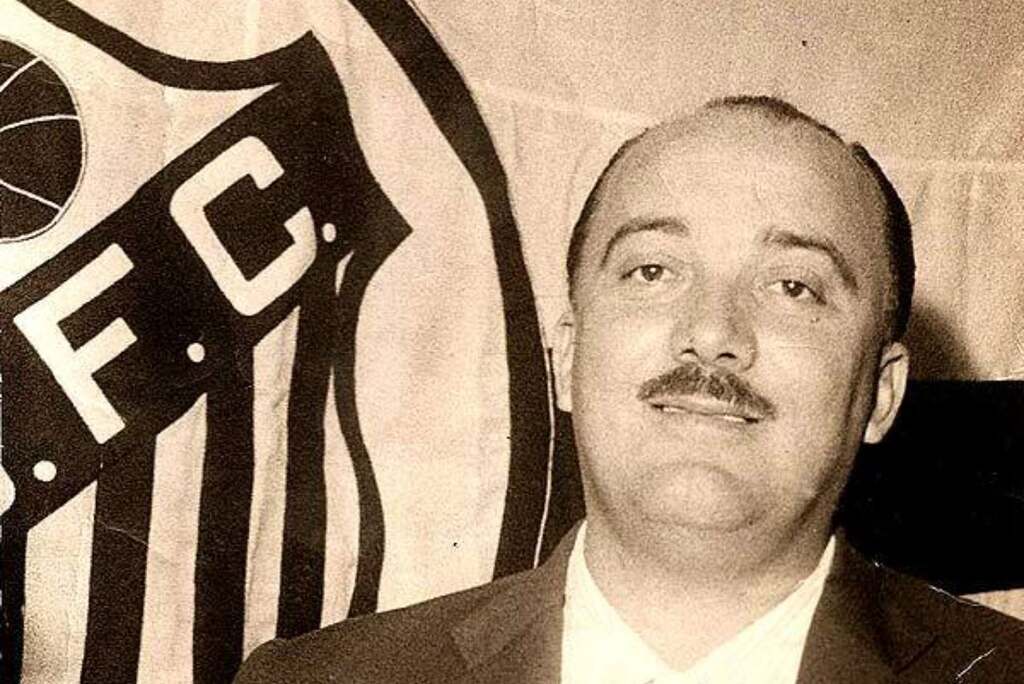 Ex-t´cnico de futebol, Lula, de roupa social em frente a uma bandeira do Santos.