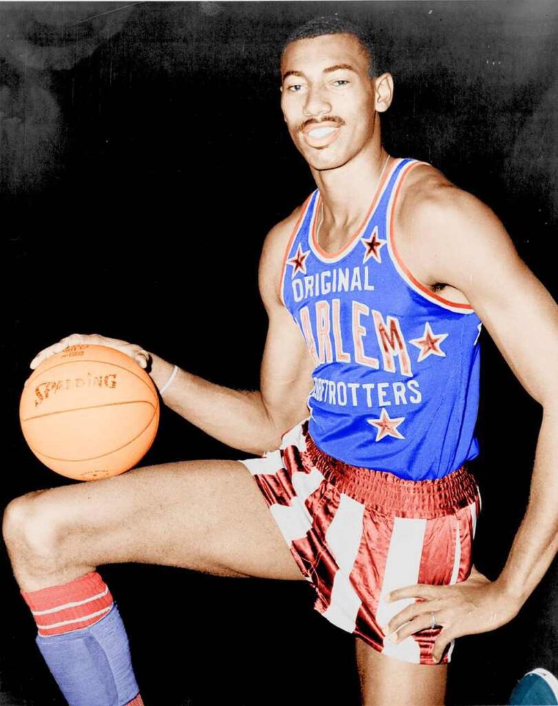 Jogador de basquete Wilt Chamberlain, vestindo calção vermelho e branco, com camisa azul.