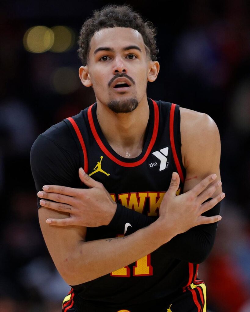 Jogador de basquete Trae Young, vestindo uniforme preto com detalhes vermelhos durante partida.