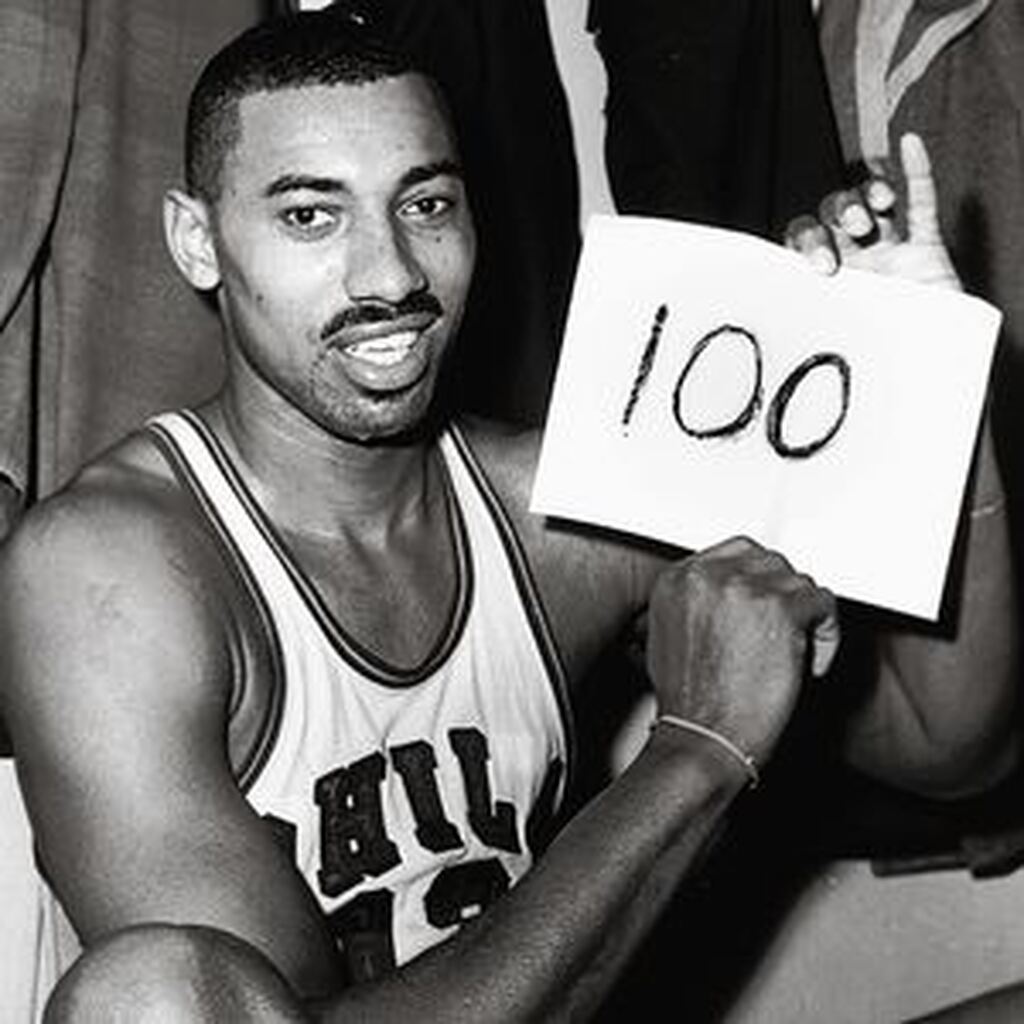 100 pontos em um só jogo Jogador de basquete de uniforme branco com letras vermelhas, segurando um papel escrito 100, em preto e branco.