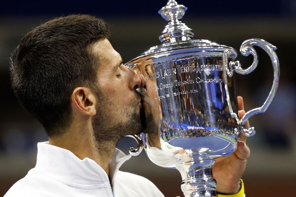 Djokovic, de camisa branca, beijando taça prateada na conquista do US Open 2023