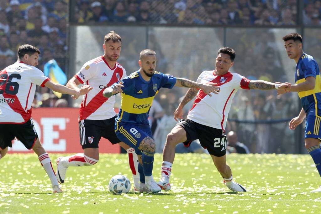 Jogador do Boca Junior conduzindo e passando no meio de dois marcadores do River Plate.