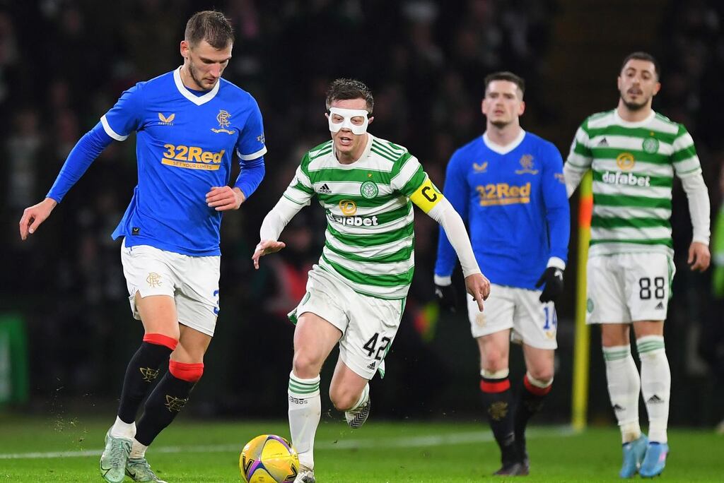 Jogador do Celtic, com máscara branca na cara, conduzindo a bola enquanto jogador adversário tenta desarmá-lo.