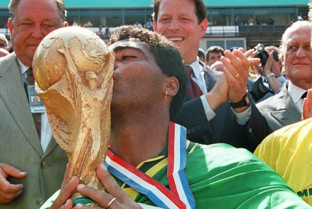 Ex-jogador de futebol Romário, erguendo e beijando a taça da Copa do Mundo com a bandeira do Brasil