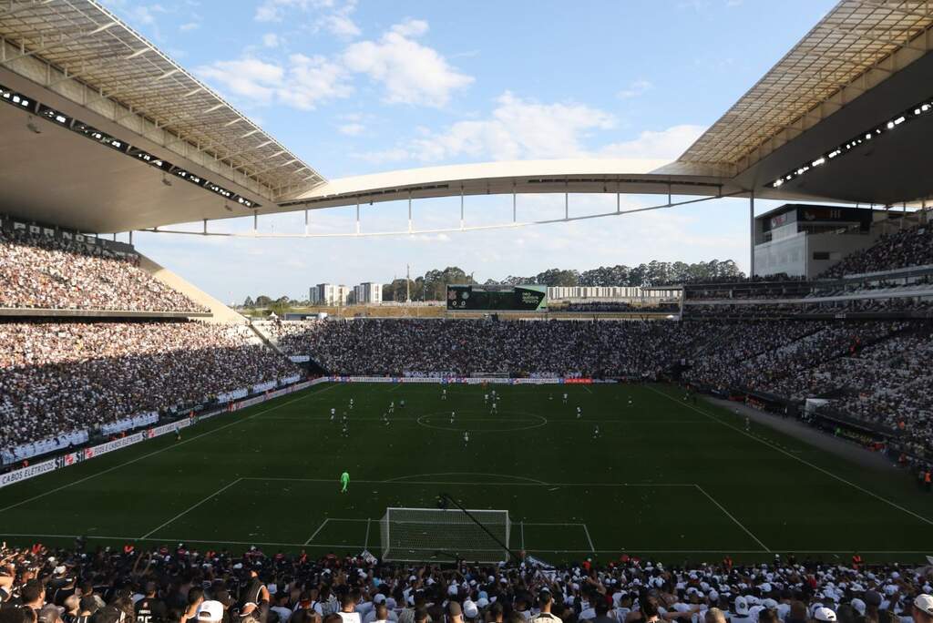 Estádio do Corinthians lotado, com a torcida ocupando toda a arquibancada em festa durante partida.