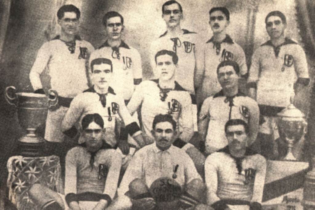 Elenco antigo do Corinthians posando para foto ao lado de uma taça, em preto e branco.