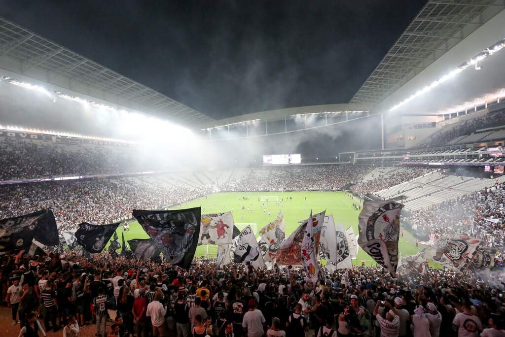 Estádio do Corinthians visto do meio de sua torcida na arquibancada, em festa durante o jogo.