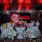 Torcida do Flamengo em festa no estádio, levantando mosaico com troféus e mascote do clube no meio da arquibancada.