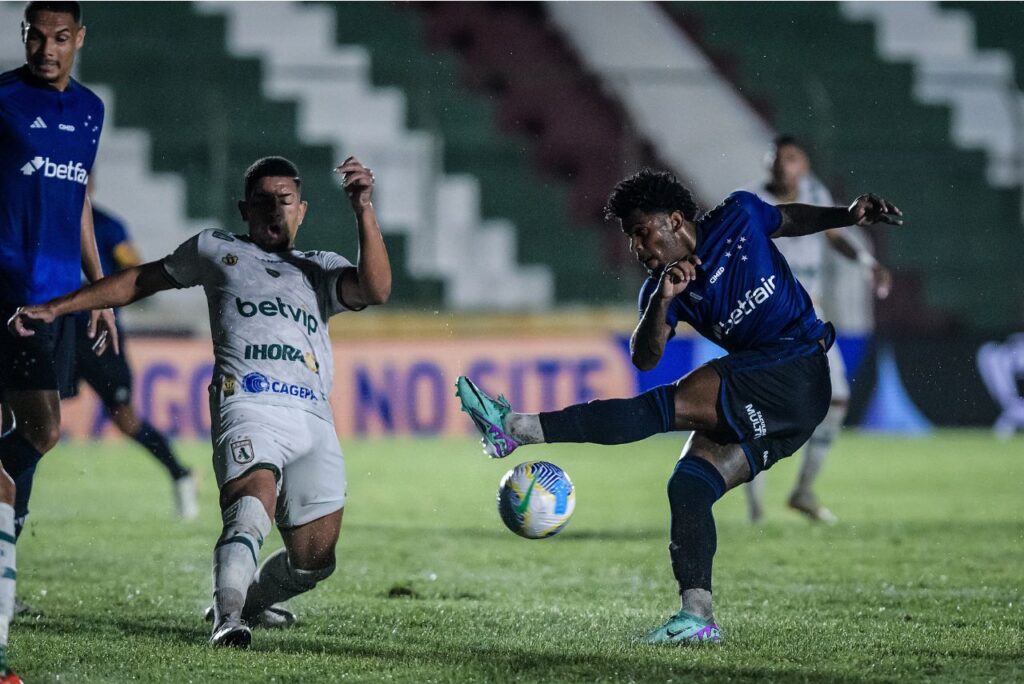 Jogador do Cruzeiro, com uniforme azul, divide a bola com um jogador do Sousa, de uniforme branco.