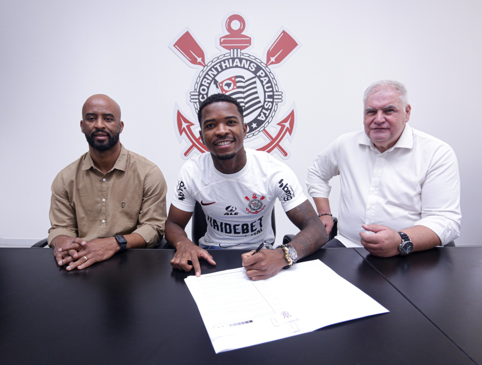 Jogador com blusa do corinthians ao lado de duas pessoas