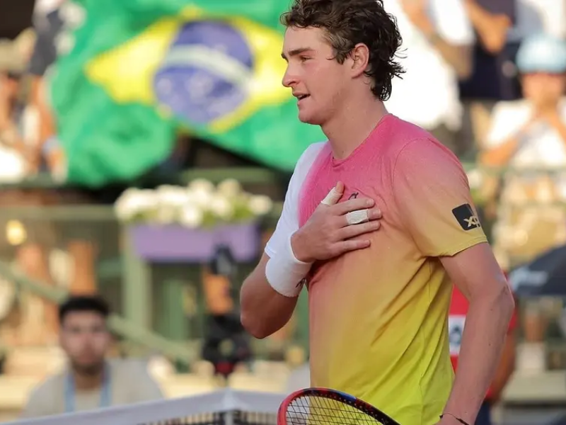 João Fonseca comemora vitória no tênis com a camisa do Brasil, demonstrando alegria e paixão pelo esporte.