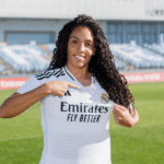 Yasmim Queiroz vestindo o uniforme do Real Madrid feminino em um estádio de futebol.