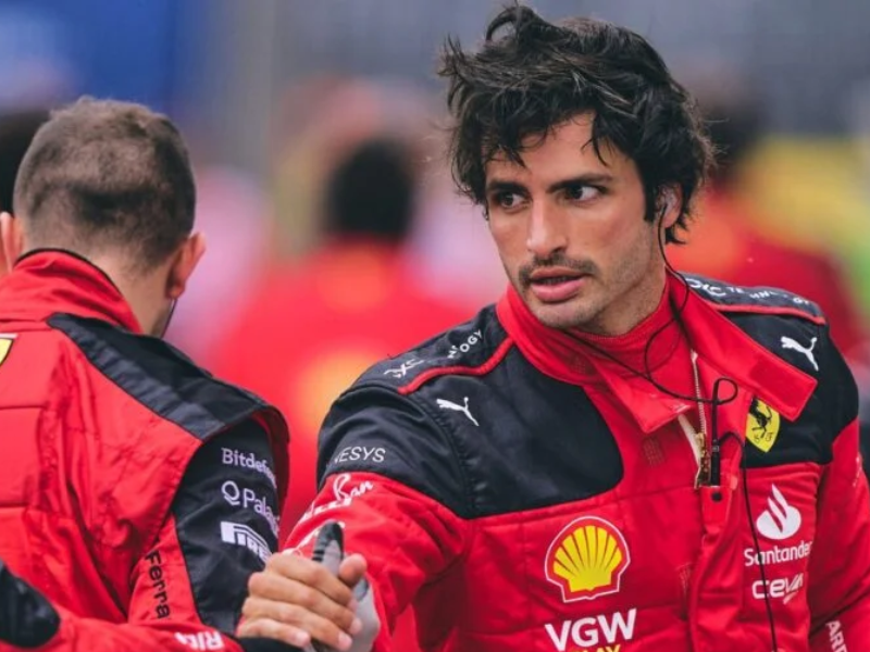 Carlos Sainz observando carro da Williams em paddock de F1.