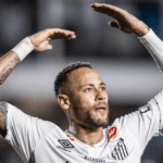 Jogador de futebol driblando em campo com grama sintética.