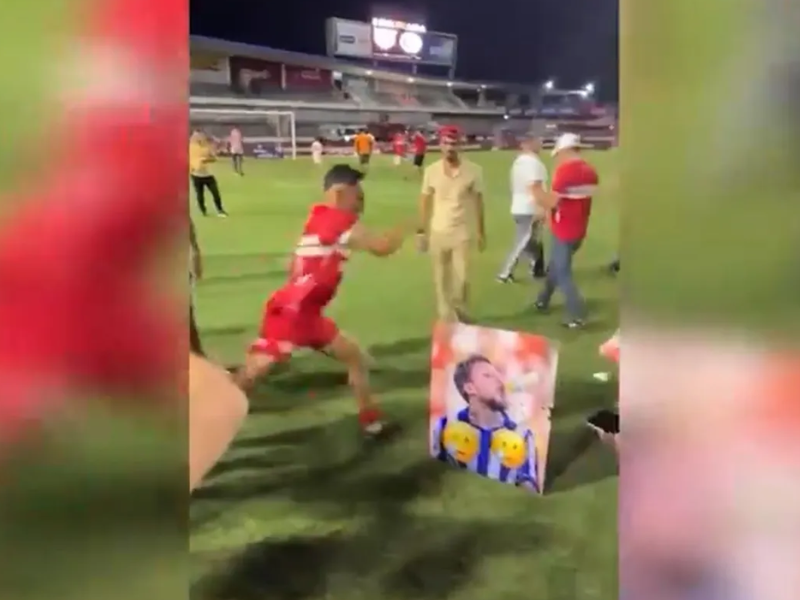 Jogador do CRB chutando foto de rival do CSA em vestiário de futebol.