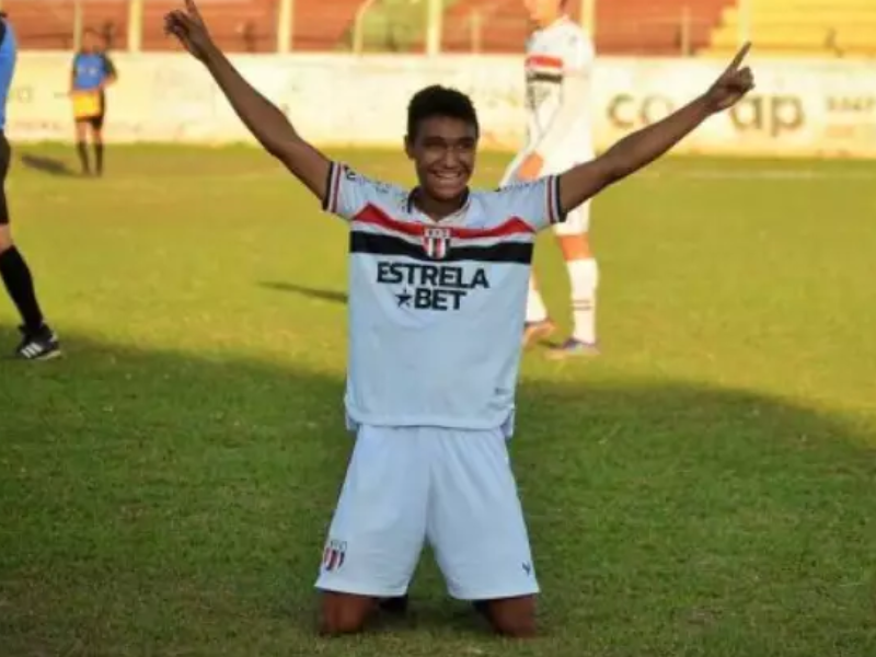 Pedro Severino sorrindo em fisioterapia, com vista para o campo de futebol.