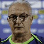Imagem de close-up de Dorival Júnior refletindo em seu escritório.