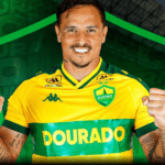 Edu sorrindo ao segurar a camisa do Cuiabá durante sua apresentação.