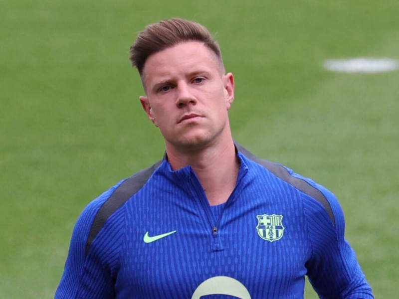 Marc-André ter Stegen, goleiro do Barcelona, sentado em um banco de fisioterapia, com expressão séria mas determinada, indicando sua recuperação após cirurgia.