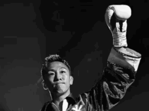 Um ringue de boxe vazio e escuro no Korakuen Hall, Tóquio, com luvas avermelhadas no chão, simbolizando luto e a tragédia.