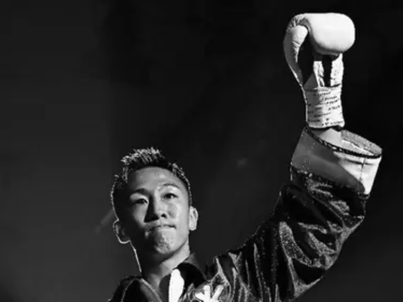 Um ringue de boxe vazio e escuro no Korakuen Hall, Tóquio, com luvas avermelhadas no chão, simbolizando luto e a tragédia.