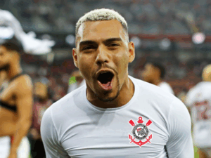 Um jogador do Corinthians, de costas, chuta uma bola de futebol em um campo iluminado, celebrando um gol crucial.