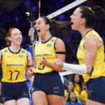 Uma jogadora de vôlei brasileira em movimento, bloqueando a bola, em uma quadra com iluminação dramática.