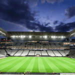 Neo Química Arena ao pôr do sol com uma mão depositando dinheiro em uma caixa de coleta para a campanha 'DOE ARENA CORINTHIANS'.